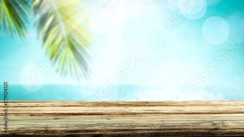 Table background with wooden board in the beautiful ocean and beach view. Palm leaves and clear sunny sky. Free space on a wooden table for an advertising product.