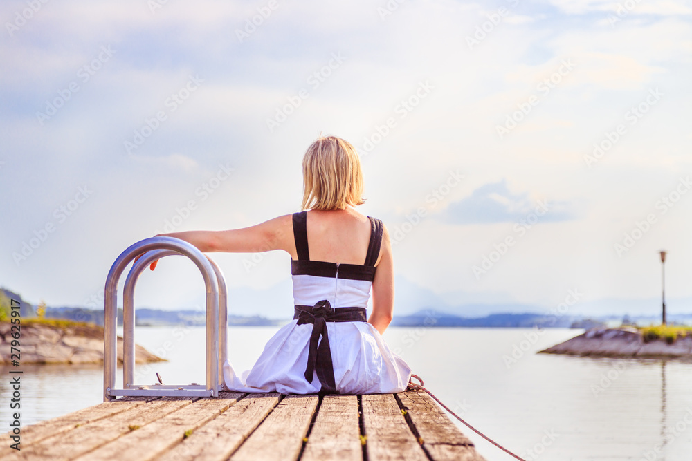 Beautiful young woman with white dress is sitting on a footbridge and enjoying the view, summer time