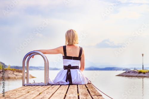 Beautiful young woman with white dress is sitting on a footbridge and enjoying the view, summer time © Patrick Daxenbichler