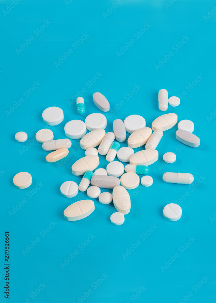 Assorted pharmaceutical medicine pills, tablets and capsules over blue background