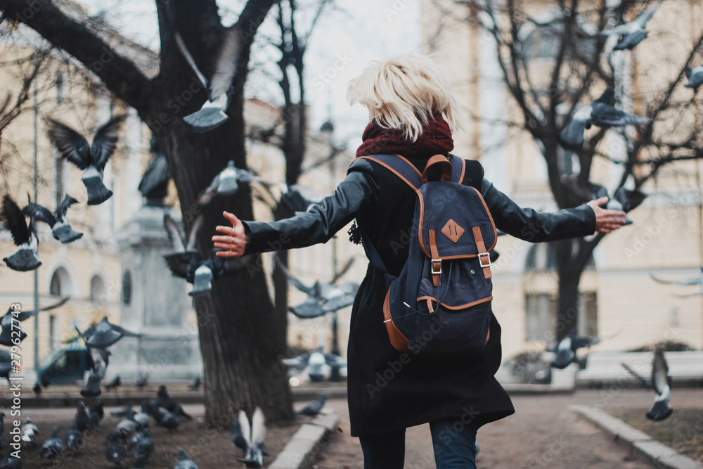 A young girl outdoors playing with lots of pigeons. Birds soar