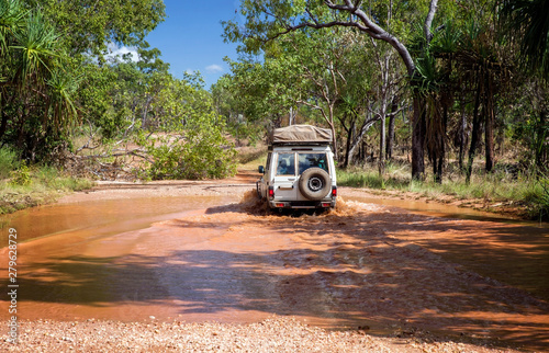 Western Australia     Flooded Outback gravel road with 4WD car crossing the waterhole at the savanna