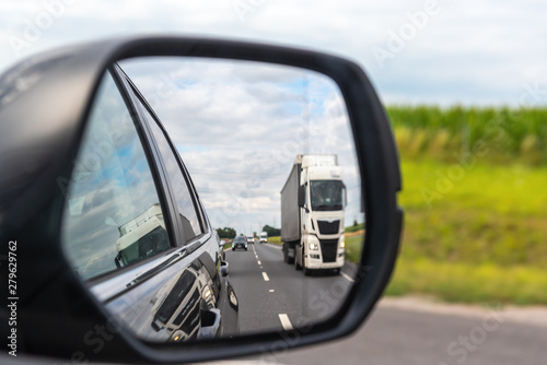 Asphalt road with truck reflected in car mirror.