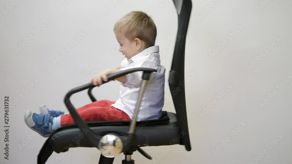 Little child sitting and spinning in a business chair, funny kid smiling Little child sitting and spinning in a business chair, funny kid smiling