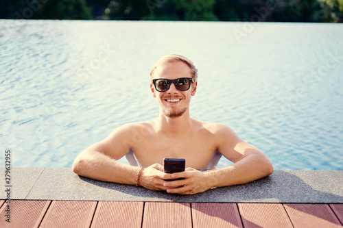 Work and relaxation. Handsome young using smartphone on swimming pool.