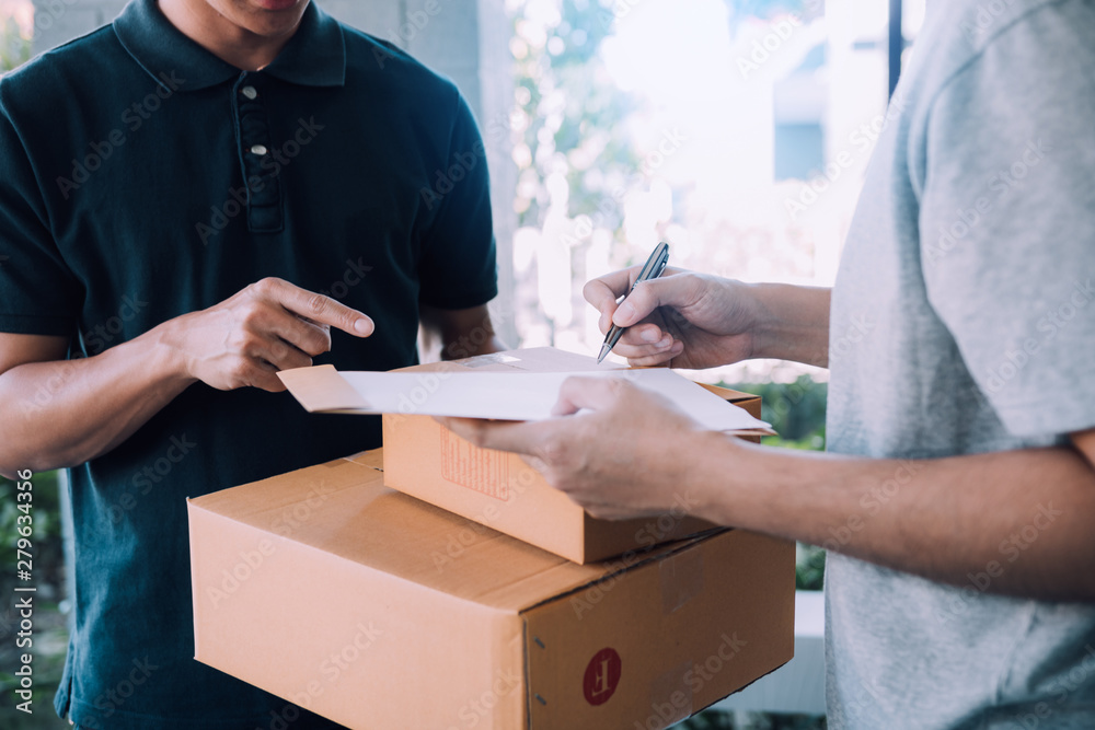 Delivery young man standing at the door of home and carrying parcels for young male to signing. Delivery young man standing at the door of home and carrying parcels for young male to signing.