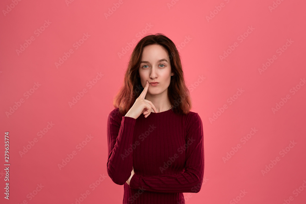 Beautiful young lady standing isolated over pink background with finger raised close to mouth expressing gesture of thoughtfulness. Beautiful young lady standing isolated over pink background with finger raised close to mouth expressing gesture of thoughtfulness.