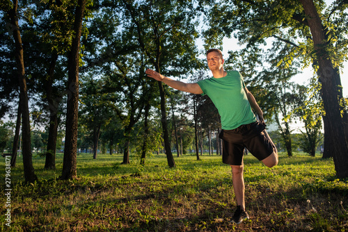 A sportsman stretching his body in a forest during warming-up for jogging