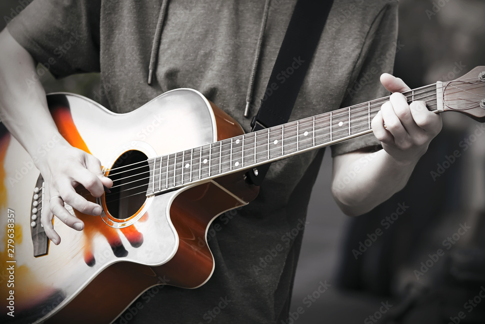 Fototapeta premium A professional musician plays an improvised melody on a six-string acoustic beautiful guitar, holding a mediator in his hand. Photo in black and white to highlight the brightness of the music