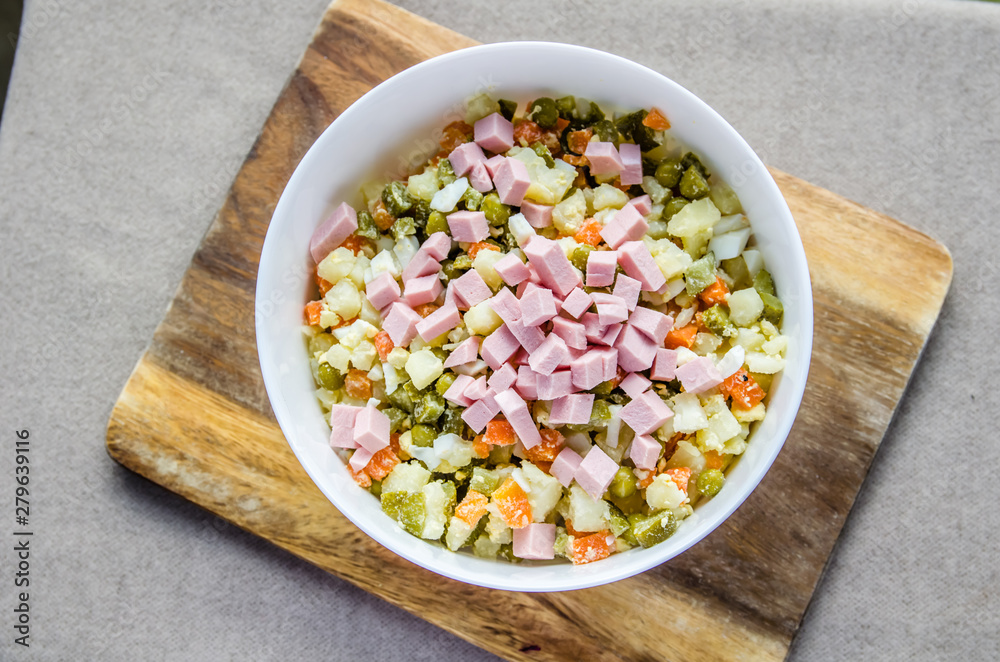 Russian salad Olivier with potato carrot green peas ham on the board and gray background