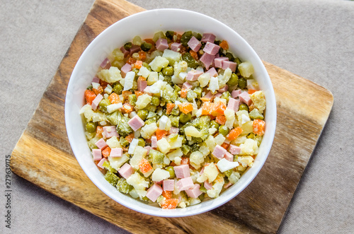 Russian salad Olivier with potato carrot green peas ham on the board and gray background