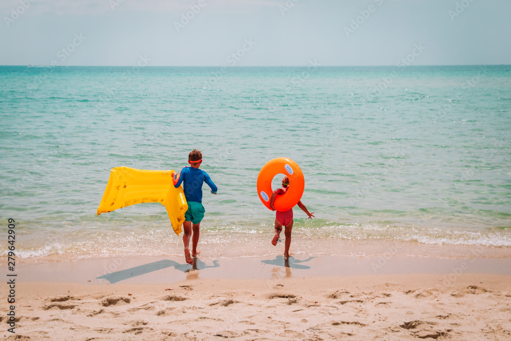 Obraz premium happy boy and girl with floaties run swim on beach
