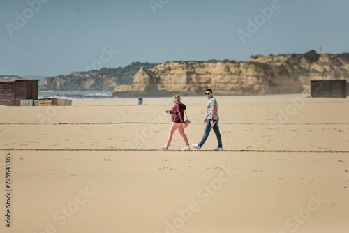 Happy young couple enjoying sunny days on the beach. Man and woman playing with sand. Love story near the ocean. Smiling attractive pair embracing and holding hands on the background of buildings.