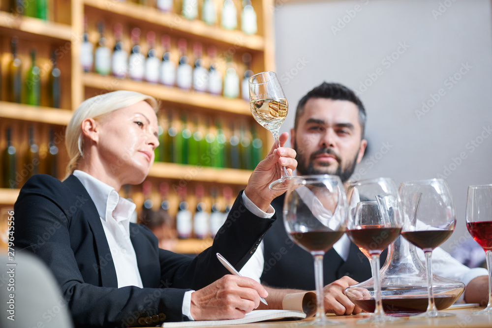 Serious professional sommeliers examining color of white wine in bokal Serious professional sommeliers examining color of white wine in bokal