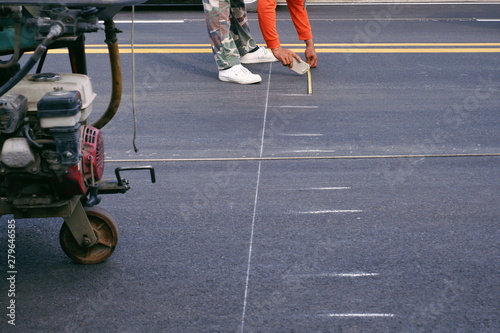 Part of road worker using measuring tape to make lines for pedestrian crosswalk painting on asphalt road surface in the city, selective  focus