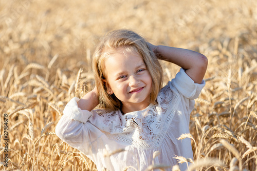 little blonde girl stands in a wheat field in summer and smiles