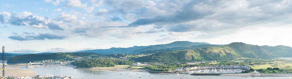 Panoramic North Wales vista over the Conwy estuary nestled below the Welsh mountains. Conwy castle and marina bathed in beautiful evening light.