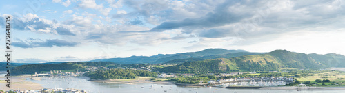 Panoramic North Wales vista over the Conwy estuary nestled below the Welsh mountains. Conwy castle and marina bathed in beautiful evening light.
