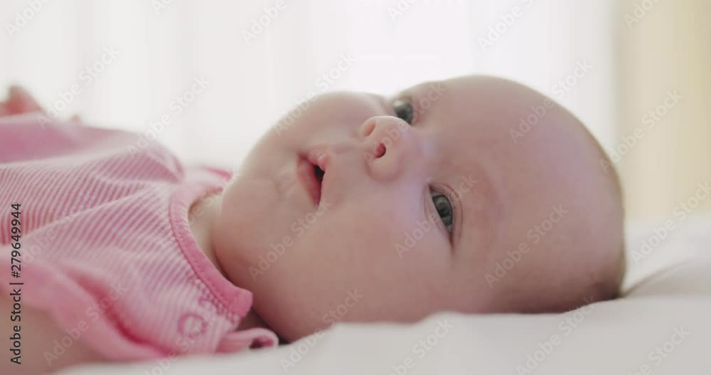 Little baby girl gurgling to herself sticking out her little tongue as she lies on her back in a cot in a close up on her face Little baby girl gurgling to herself sticking out her little tongue as she lies on her back in a cot in a close up on her face