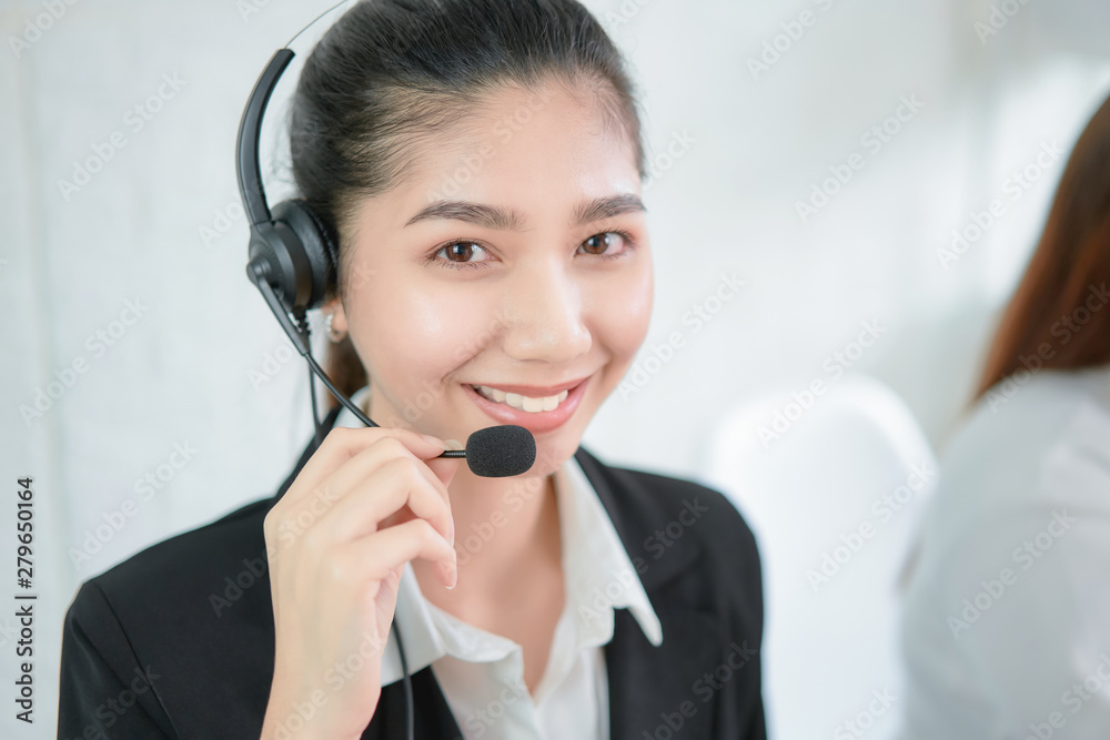 Smiling Asian businesswoman consultant wearing microphone headset of customer support phone operator at workplace. Smiling Asian businesswoman consultant wearing microphone headset of customer support phone operator at workplace.