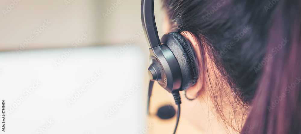 Back view of woman consultant wearing microphone headset of customer support phone operator at workplace. proportion of the banner for ads. - obrazy, fototapety, plakaty 