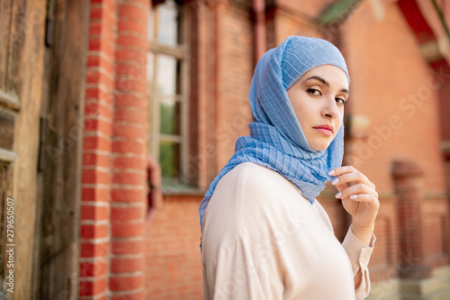 Leinwand Poster Young serious Arabian female in blue hijab chilling out in ancient city