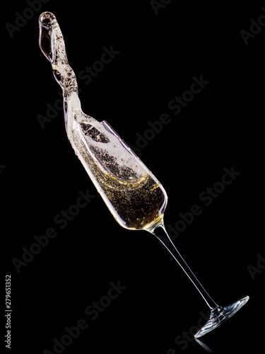 Glass for champagne with bubbles and splashes isolated on black background.