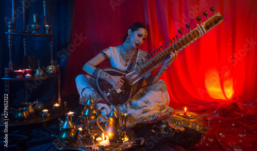 Beautiful young indian woman in traditional Sari clothing with Oriental Jewelry Playing the Sitar. photo