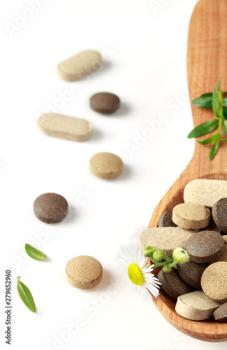 herbal pills in a wooden spoon for alternative medicine and ayurveda for health on a white background close-up