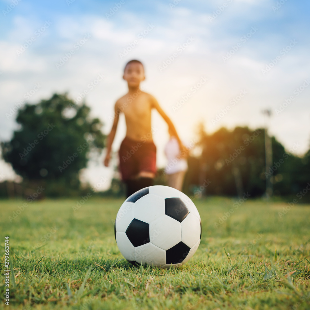 Action sport outdoors of kids having fun playing soccer football for exercise in community rural area under the twilight sunset sky. Fresh and vibrant image with anonymous people.