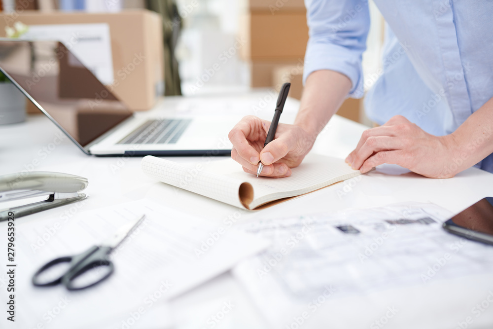 Female manager of online shop making notes on blank page of notebook Female manager of online shop making notes on blank page of notebook