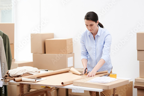 Manager of online shop office cutting wrapping paper by workplace