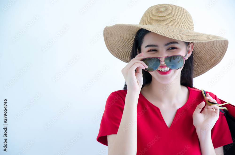 Young beautiful fashionable Asian woman holding shopping bags wearing red dress, sunglasses and hat over white background studio shot with smiling