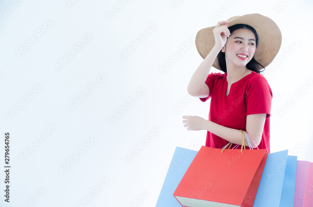 Young beautiful fashionable Asian woman holding shopping bags wearing red dress and hat over white background studio shot. Young beautiful fashionable Asian woman holding shopping bags wearing red dress and hat over white background studio shot.