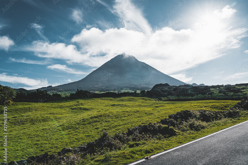 Fototapeta premium Straight EN3 longitudinal road northeast of Mount Pico and the silhouette of the Mount Pico along , Pico island, Azores, Portugal.