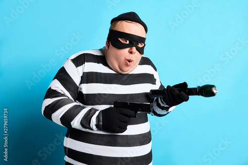 funny fat thief in striped clothes are going to commit a crime. isolated blue background. studio shot photo