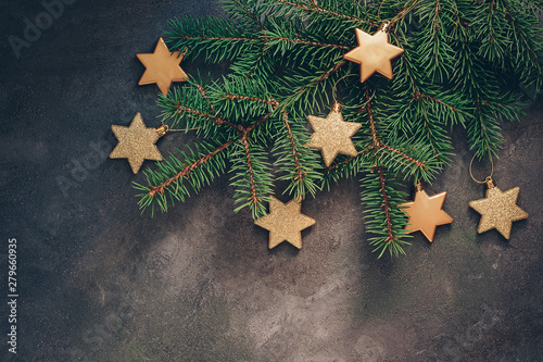 Fir-tree branches decorated with gold stars on a dark textured rustic background. Christmas holiday composition. View from above,flat lay, copy space.