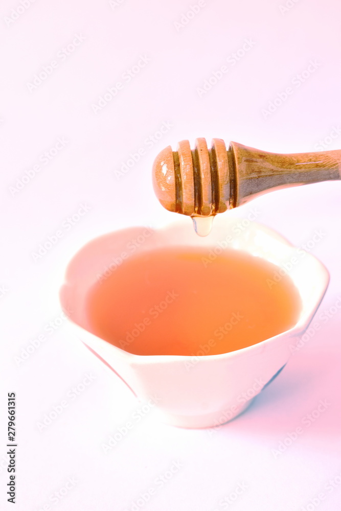 honey on wooden scoop drop to cup in white background honey on wooden scoop drop to cup in white background