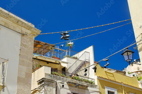 Old shoes hanging in electric wires as seen on the streets of old center of Syracuse, A bright blue sky as a background.