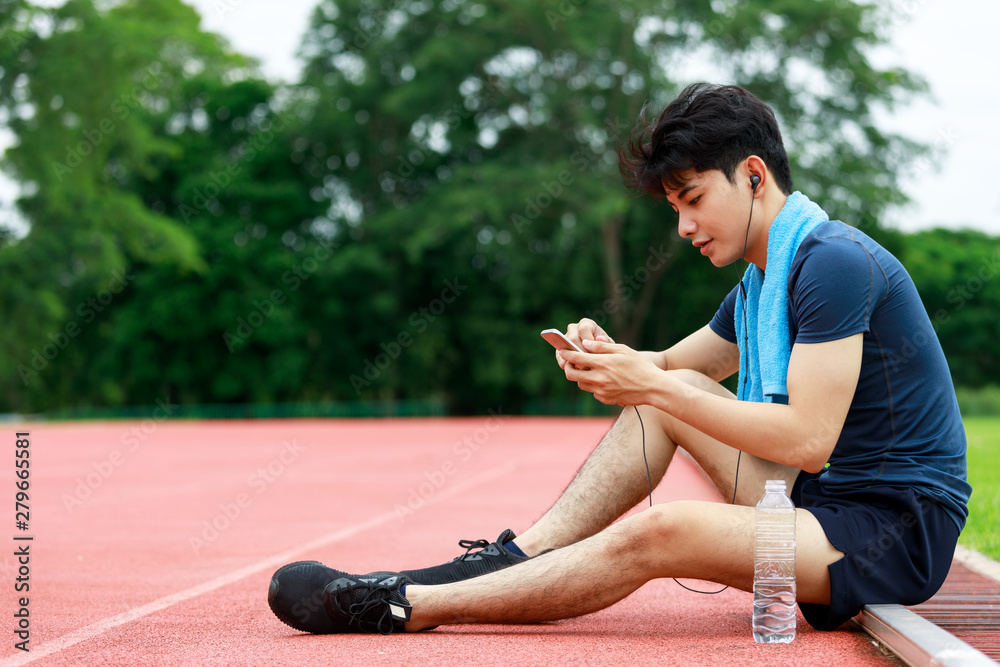 Young Asian athletic man sitting and listening music from mobile phone to relax during rest