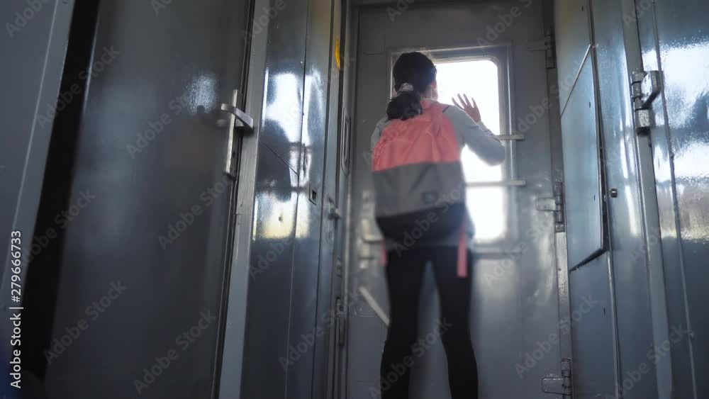 little teenage girl is backpacker traveling by train. travel transportation railroad concept. tourist school girl in the train wagon with lifestyle backpack looking out the window waving his hand little teenage girl is backpacker traveling by train. travel transportation railroad concept. tourist school girl in the train wagon with lifestyle backpack looking out the window waving his hand