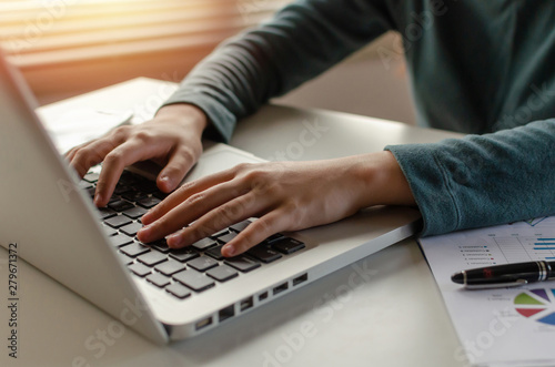 close up hand on keyboard of young woman typing working and using laptop and document on desk at home office, searching web, social network, online, finance, investment and digital technology concept