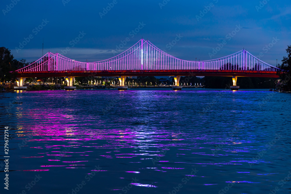 Fototapeta premium The city lights of Surat Thani at twilight with the Bridge and reflection over the Tapee River in Surat Thani , Thailand