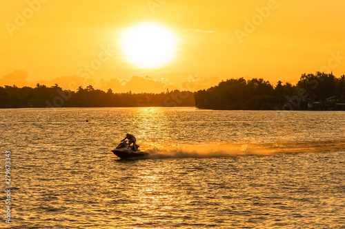 SURAT THANI, THAILAND, JULY 14, 2019: Silhouette man drive on the jet ski above the water at sunset in Surat Thani, Thailand.. © somchairakin