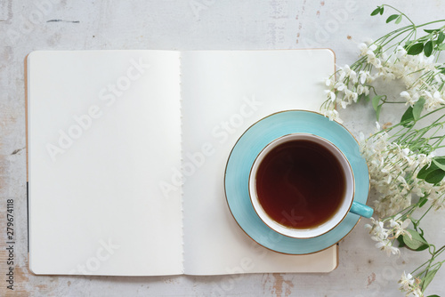 Open blank page book with a copy space and cup of tea on a white wooden table background.
