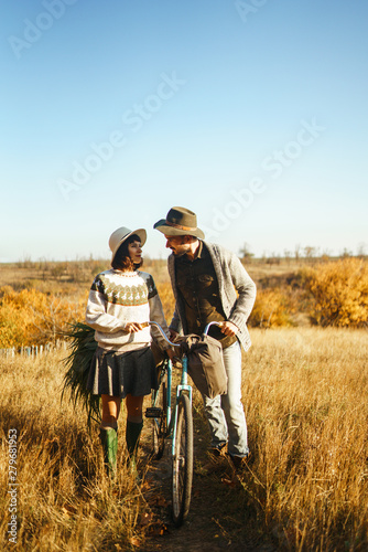 Lovely hipster couple with bike . Couple wearing beautiful hats and sweaters. Lifestyle, happy couple of two play on a sunny day in the park. The concept of youth, love and lifestyle. Sunset in autumn © maxbelchenko