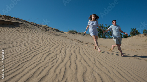 pair of young people in love run in the sand dunes.