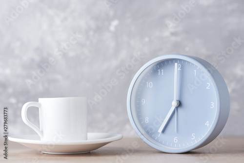 Classic alarm clock and white coffee cup on a gray background