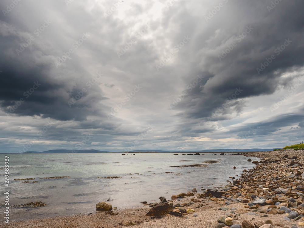 Dramatic sky over Galway bay, Atlantic ocean, Burren in the background. Calm water.