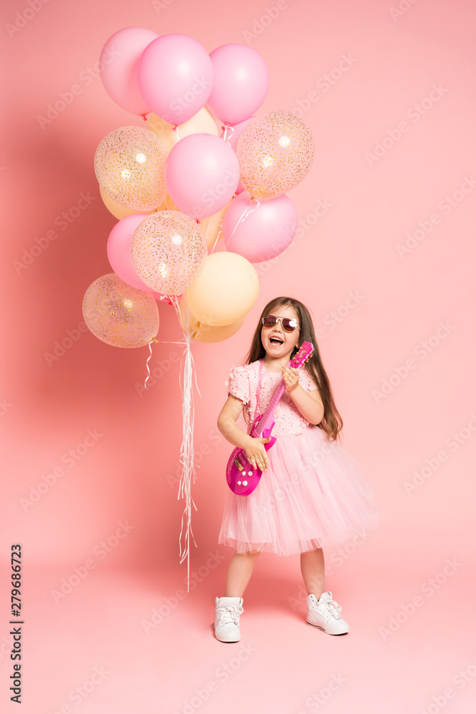 Laughing fashion little girl having fun with guitar isolated on pink background. Laughing fashion little girl having fun with guitar isolated on pink background.